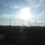 Stromleitungen und Windräder vor den Toren Berlins in aufgehender Sonne