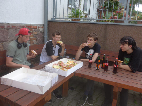 Vier junge Männer essen halbe, belegte Brötchen an einem Tisch